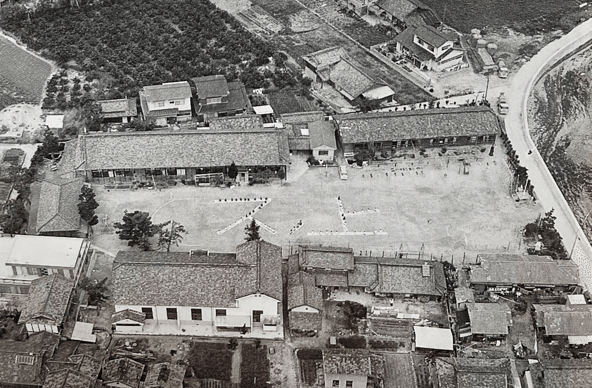 Historical aerial photograph showing the original Kaku-Mei-Sha (the hipped-roof building at left), then part of Sunoue Elementary School / 旧格明舎が写る航空写真。左の寄棟屋根の建物が格明舎