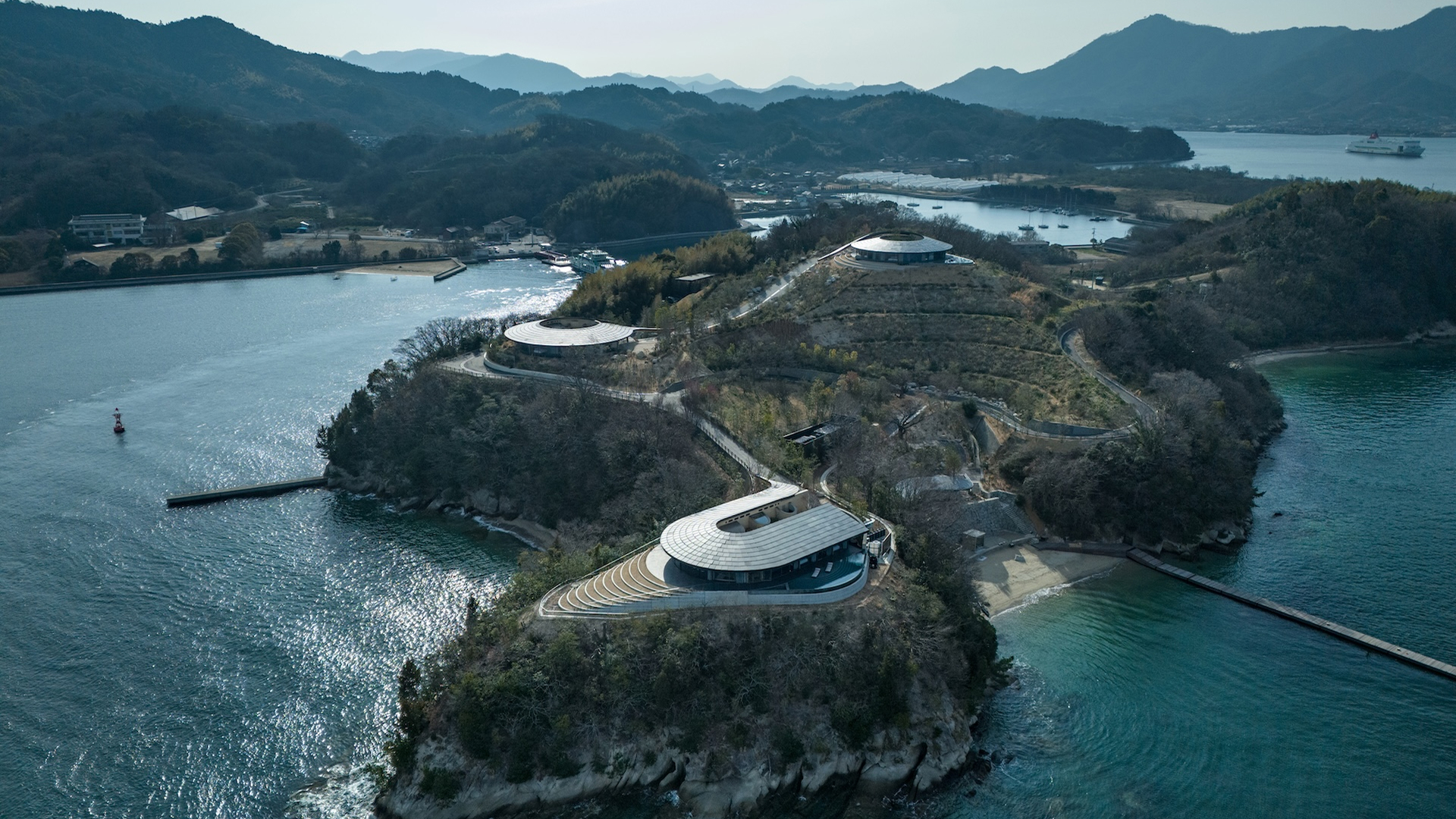 Aerial view of the three NOT A HOTEL SETOUCHI villas on the southwestern cape of Sagishima, their disc-shaped roofs set into the headland above the Seto Inland Sea.