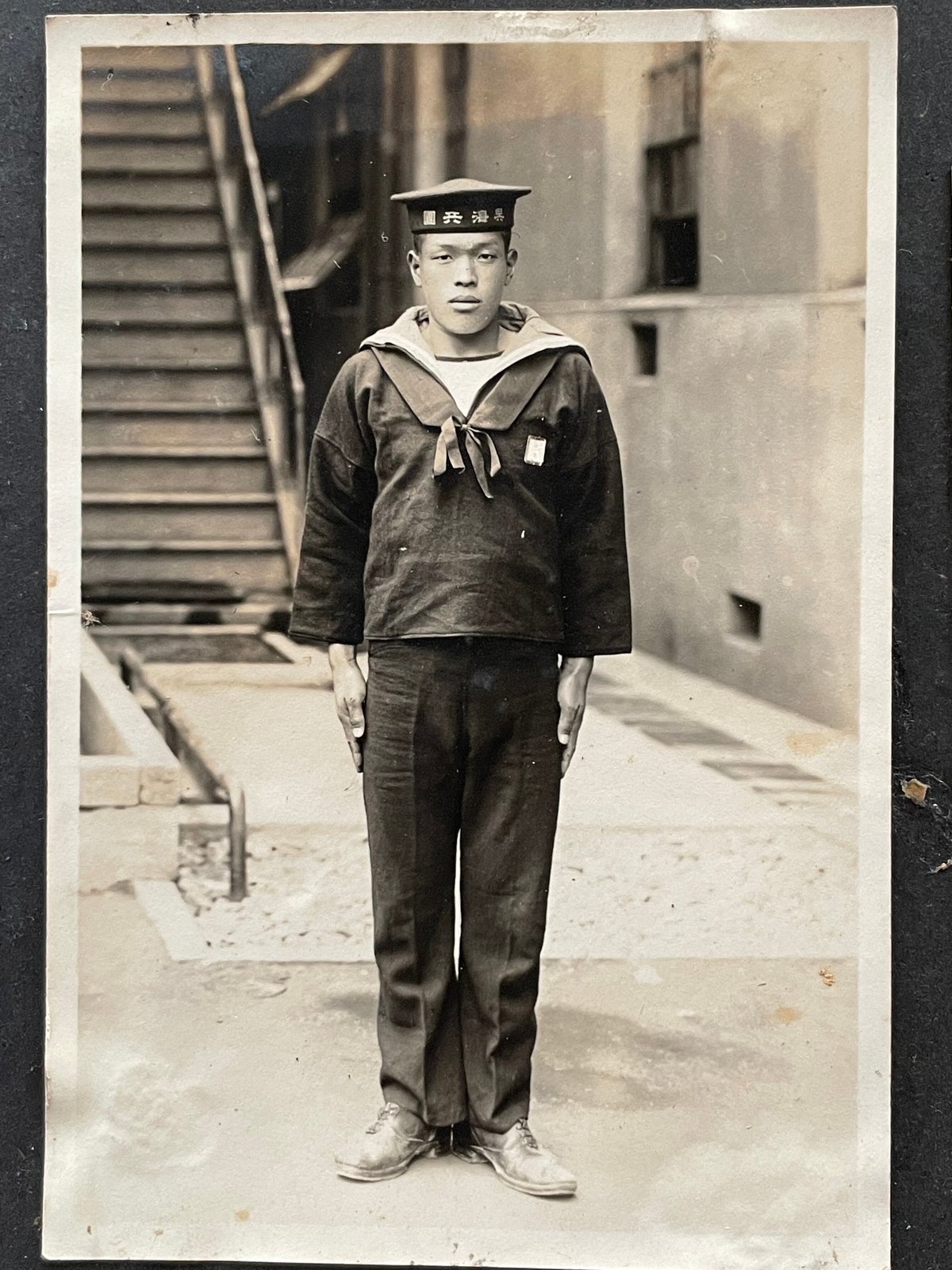 An archival Hamamoto family photograph: a young man of the family in naval-corps (海兵團) uniform. The exact individual is not confirmed; the family's maritime life is the thread that runs from the Sumifuku-maru to the house. / 浜本家の古写真、海兵團の制服姿の青年（人物の特定は未確認）