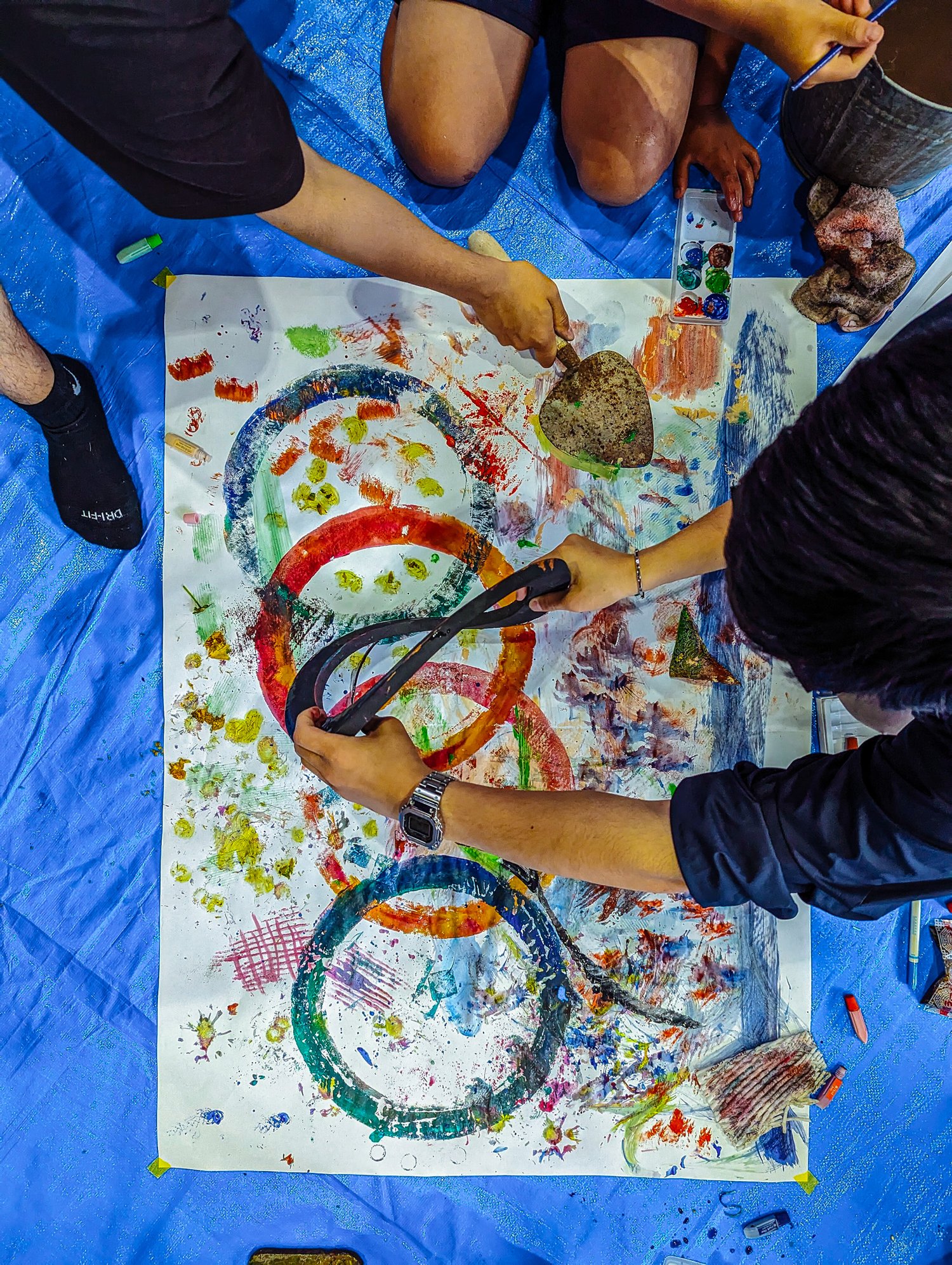 Overhead view of the cohort stamping the deconstruction ceremony's graphic language onto paper: looping circles and figure-eights printed in many colors, using a salvaged object as a stamp. 解体の儀式の図像言語を紙に刷る様子を真上から見たところ。再生材を版に用い、輪や八の字を色とりどりに刷っている。